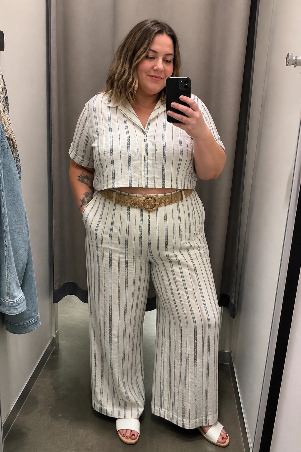 Woman in striped crop top and pants holding phone for mirror selfie in fitting room