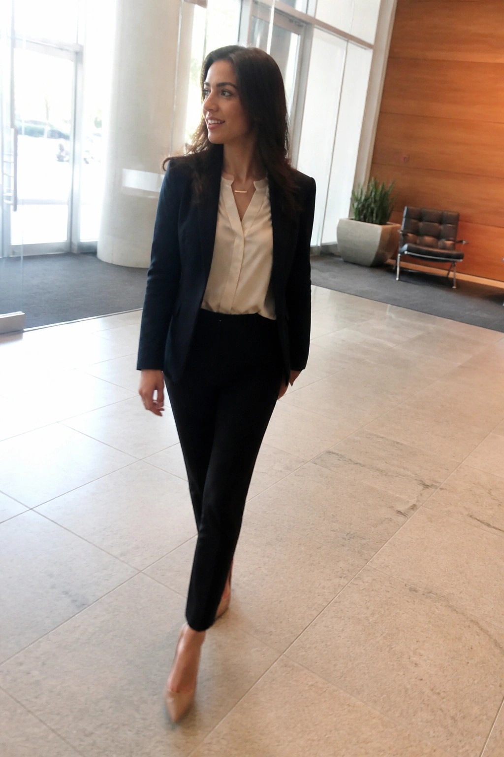 Woman in navy blazer and cream blouse walks through modern marble lobby
