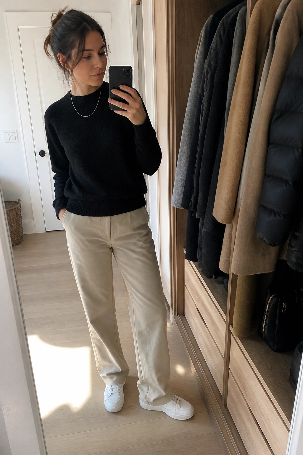 Woman in black sweater and beige pants taking mirror selfie in closet