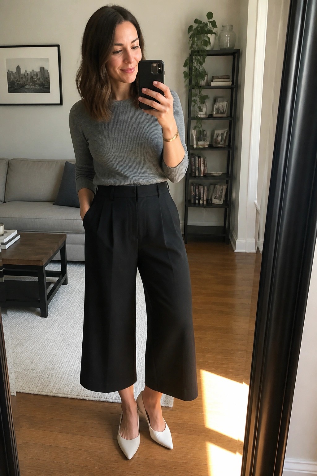 Woman in gray sweater and black wide-leg pants taking mirror selfie.