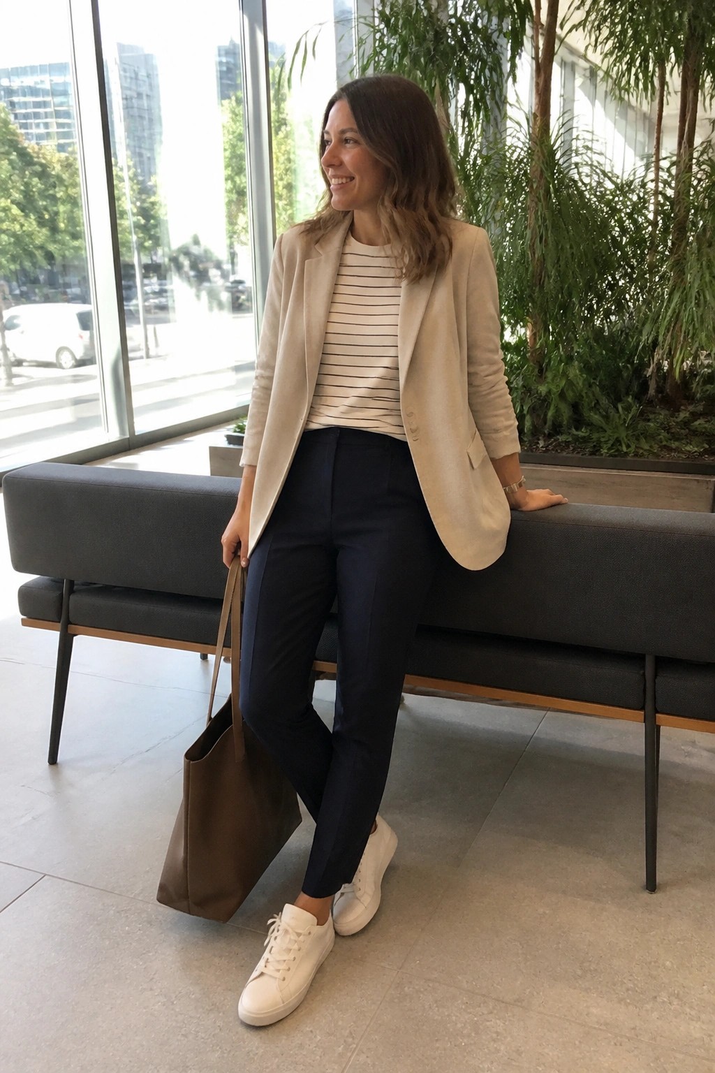 Woman in beige blazer and striped top with navy pants holding brown tote bag.