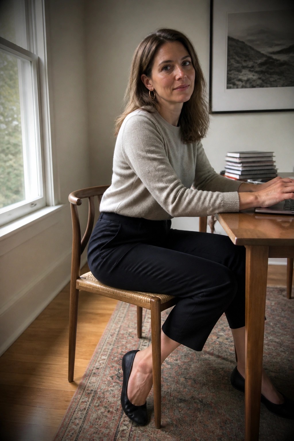 Woman in beige sweater and black pants at wooden desk with laptop