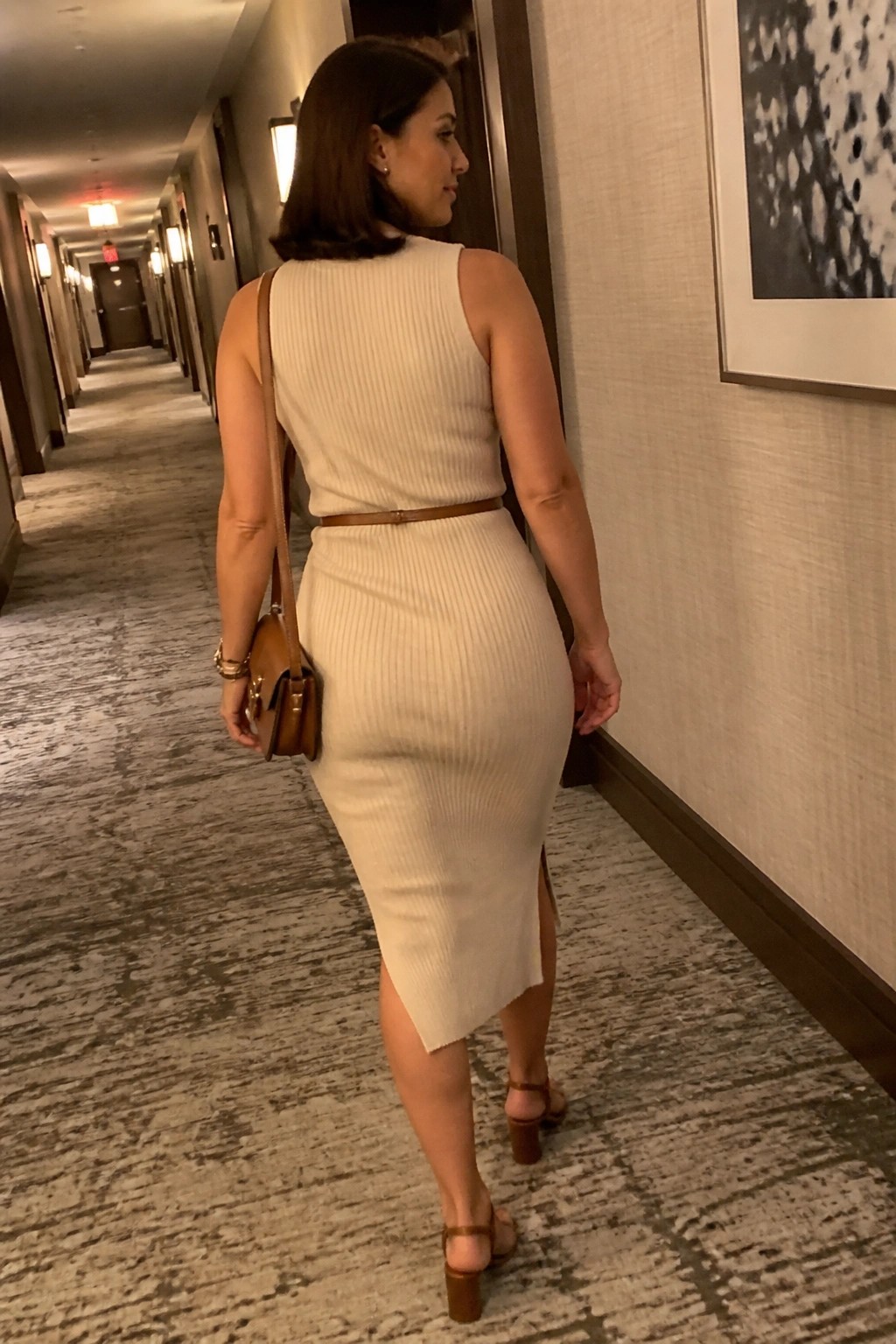 Woman in cream ribbed dress with brown belt and bag walking in hallway