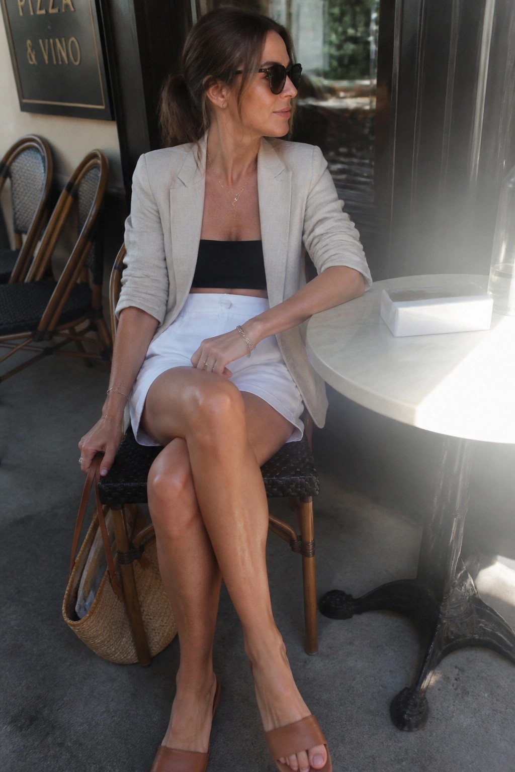 Woman in beige blazer and white shorts seated at sunny outdoor cafe table