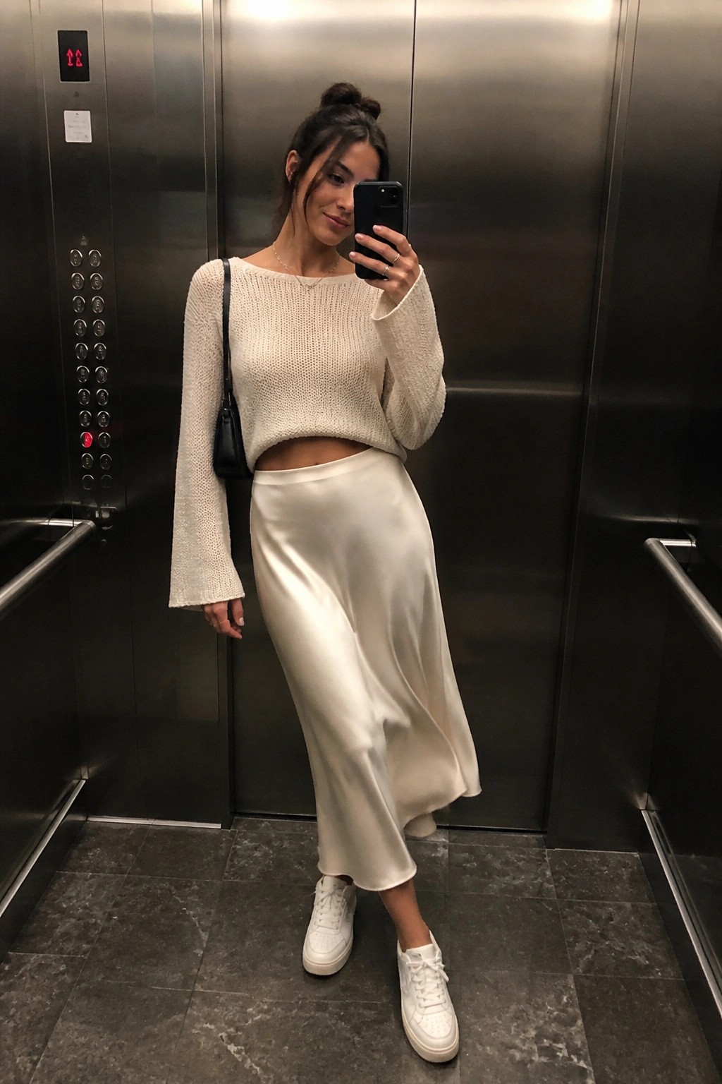 Woman in white knit sweater and satin skirt taking elevator selfie