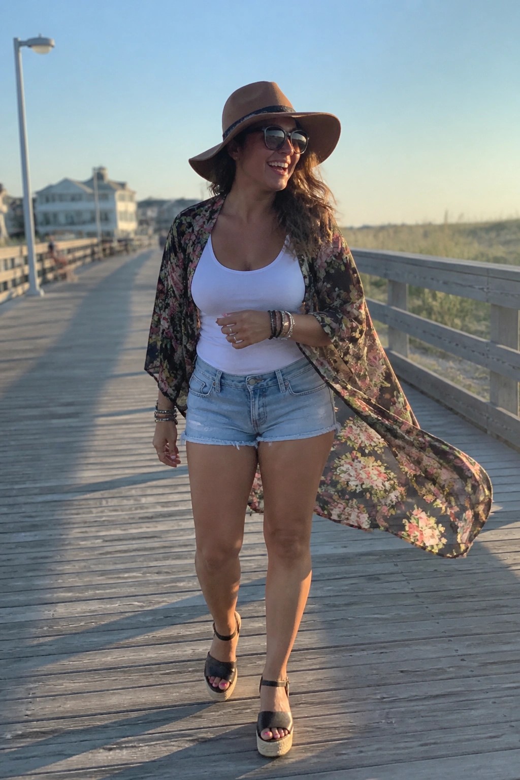 Woman in floral kimono, white tank, and denim shorts on sunny boardwalk