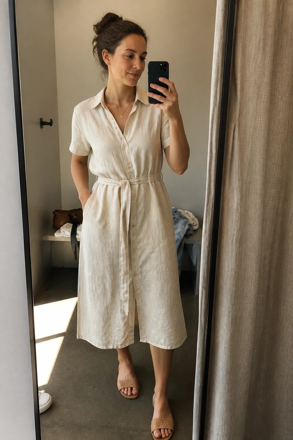 Woman in cream linen shirt dress taking mirror selfie with smartphone