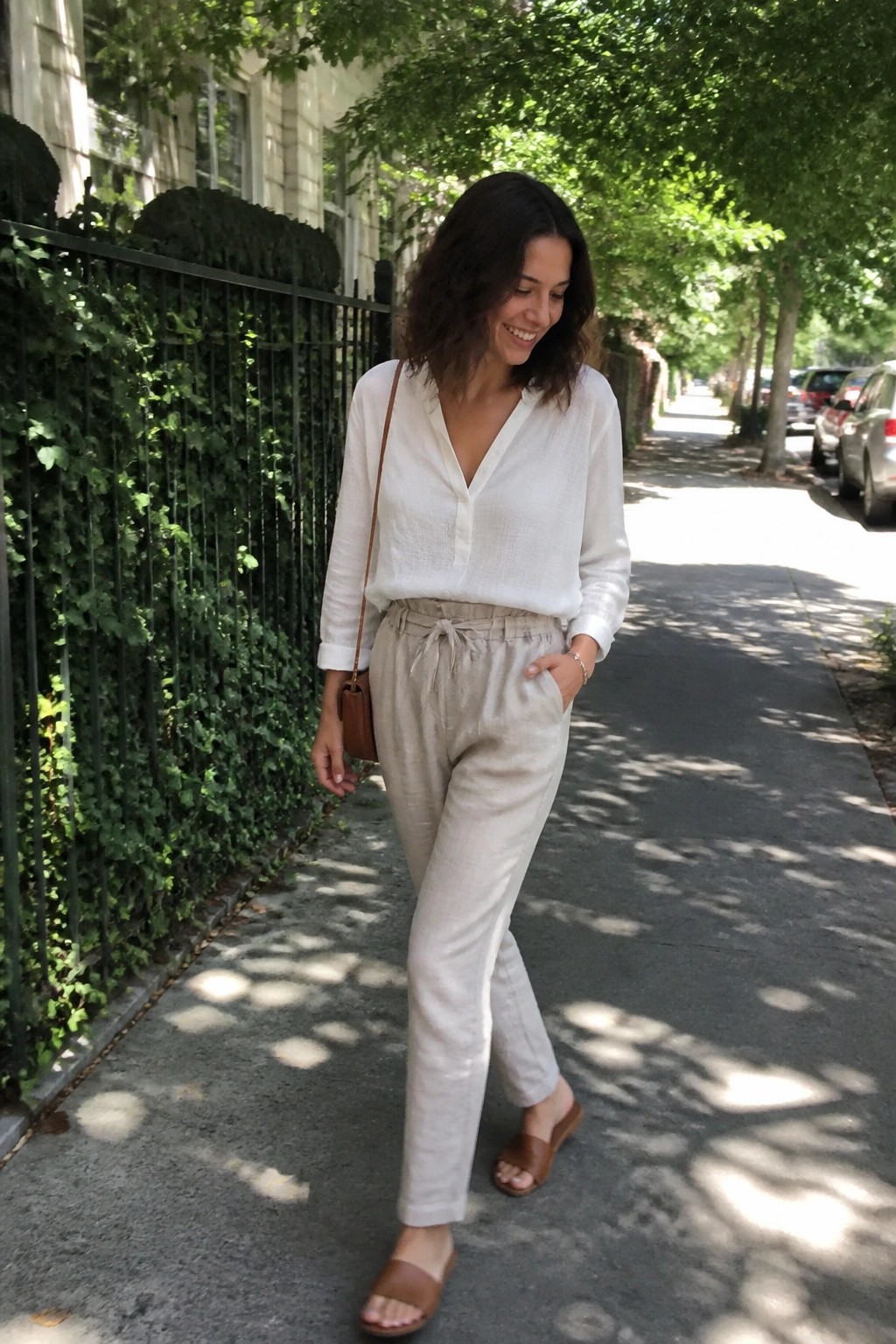 Woman smiling in white blouse and beige pants on sunny sidewalk