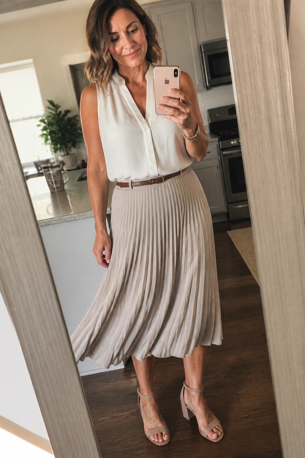 Woman in white sleeveless blouse and beige pleated skirt taking mirror selfie