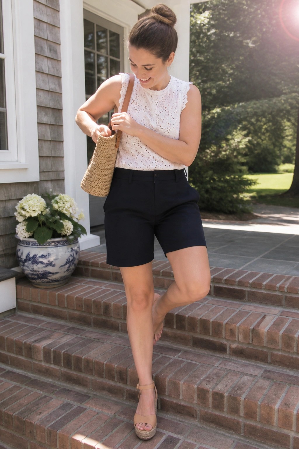 Woman in white eyelet top and black shorts holding woven bag on brick steps