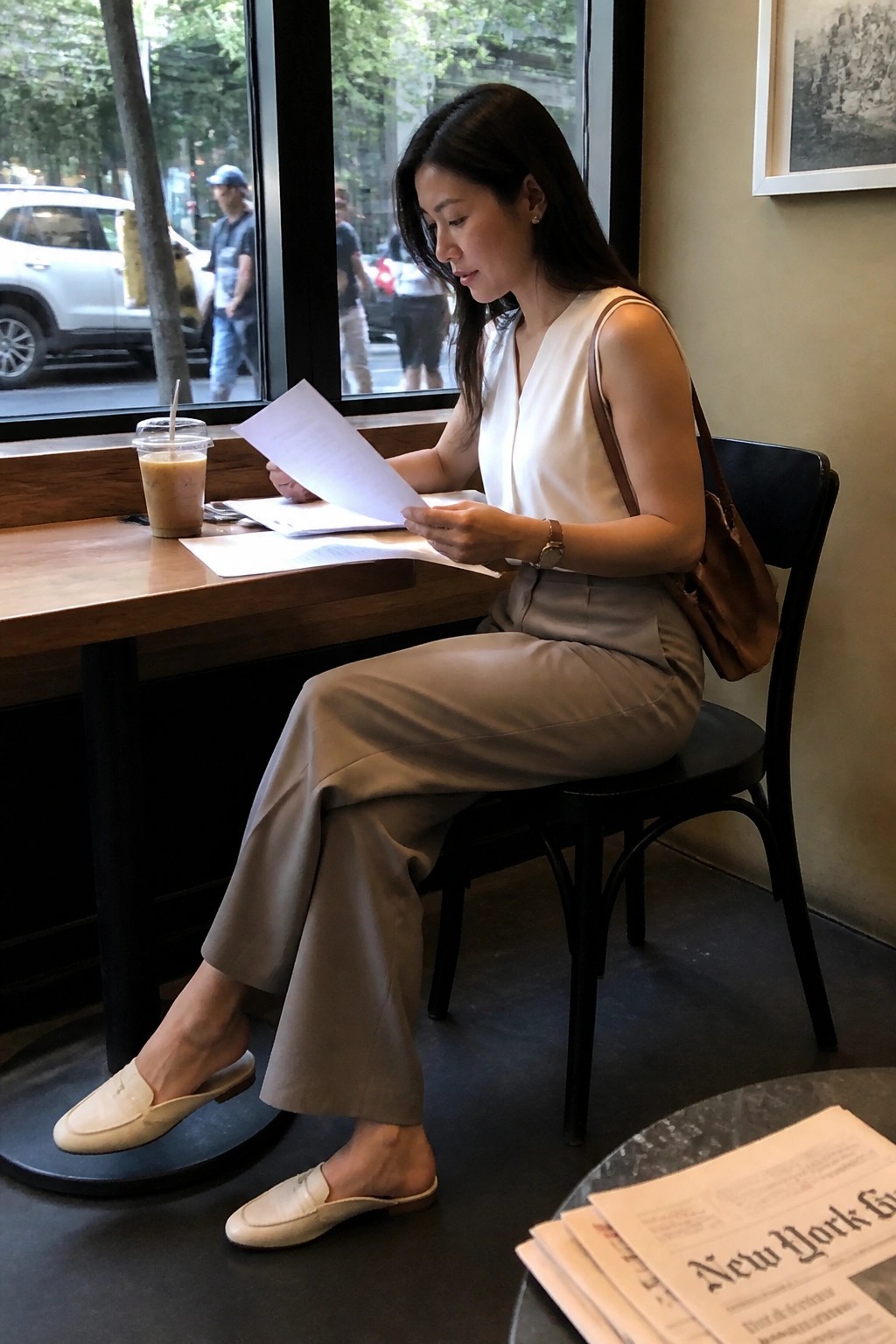 Woman in white top and beige pants reading papers at cafe table