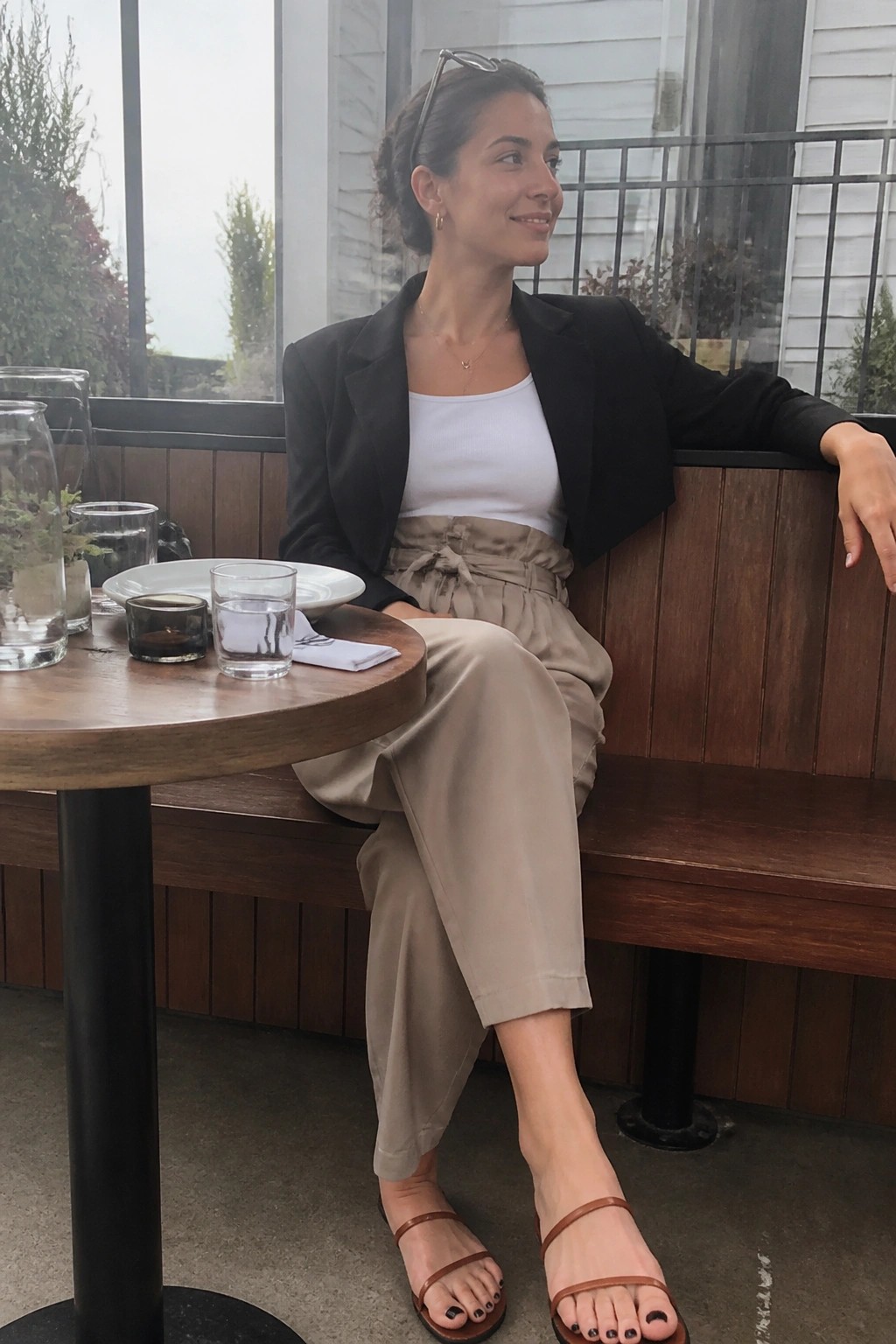 Woman in black blazer and beige pants seated at wooden cafe table