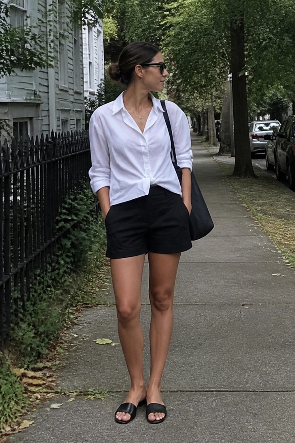 Woman in white tied shirt and black shorts on tree-lined city sidewalk