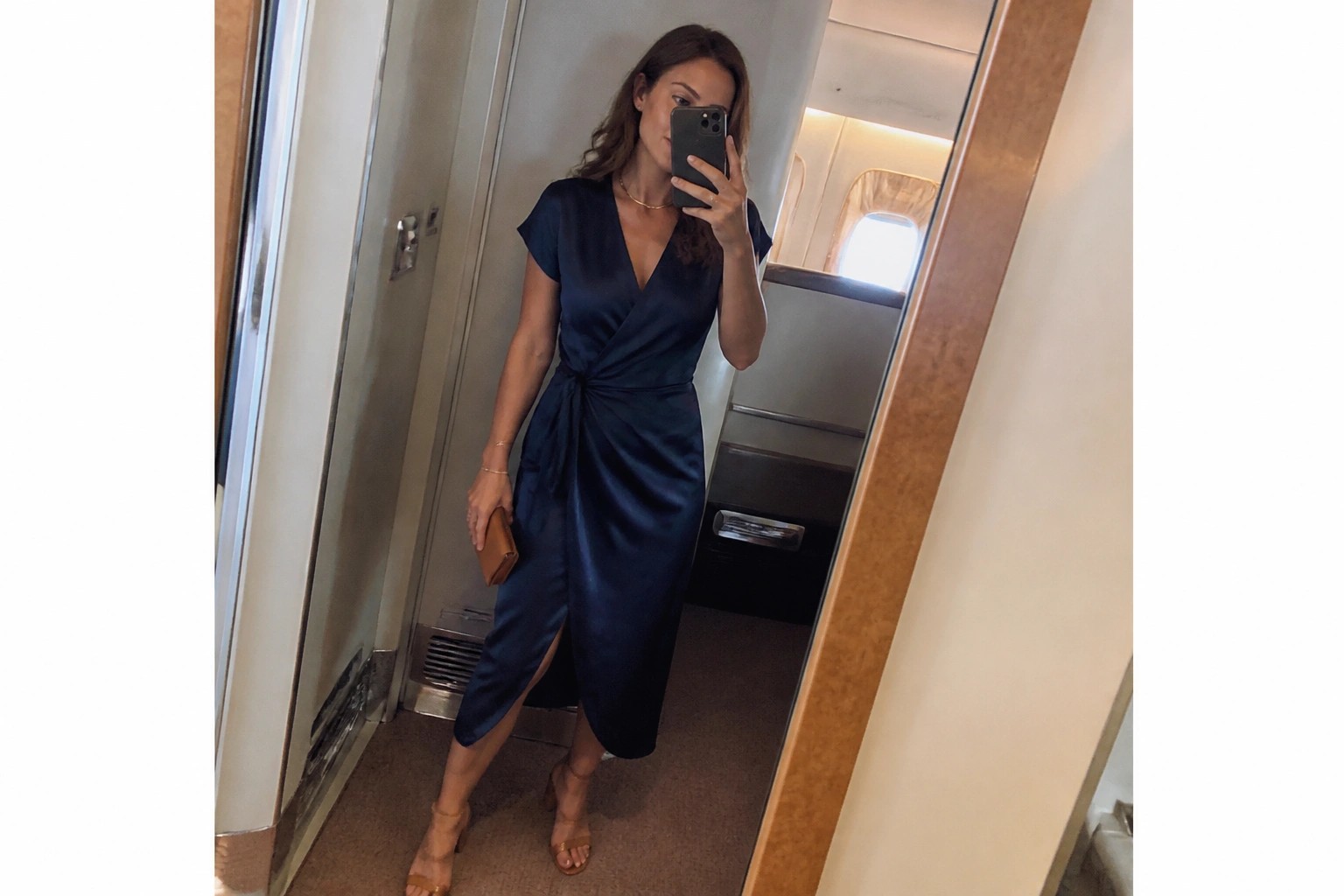 Woman in navy satin wrap dress taking mirror selfie wearing black heels