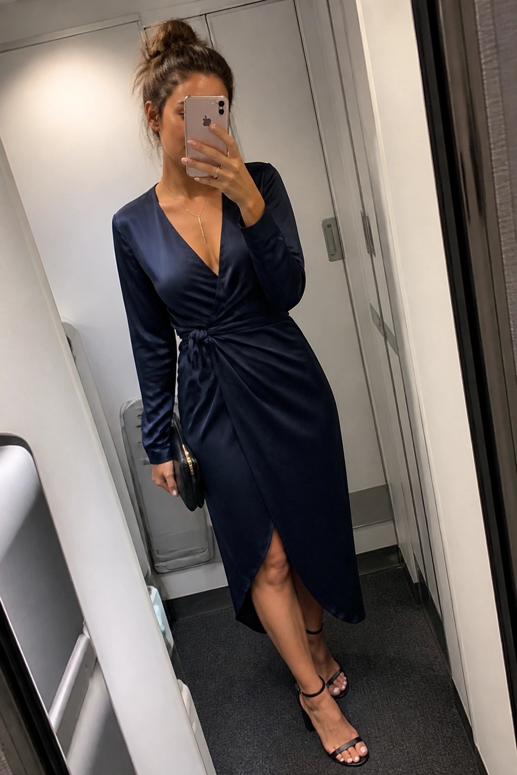 Woman in navy satin wrap dress taking mirror selfie wearing black heels