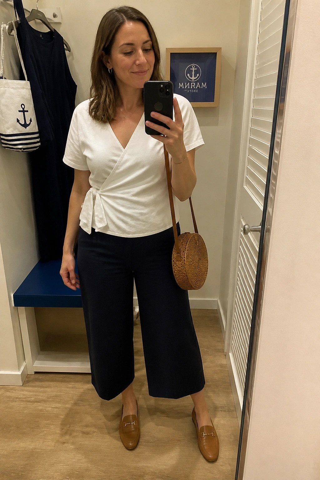 Woman in white wrap top and navy wide-leg pants taking mirror selfie in fitting room