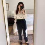 Woman in cream blouse and navy trousers taking bedroom mirror selfie