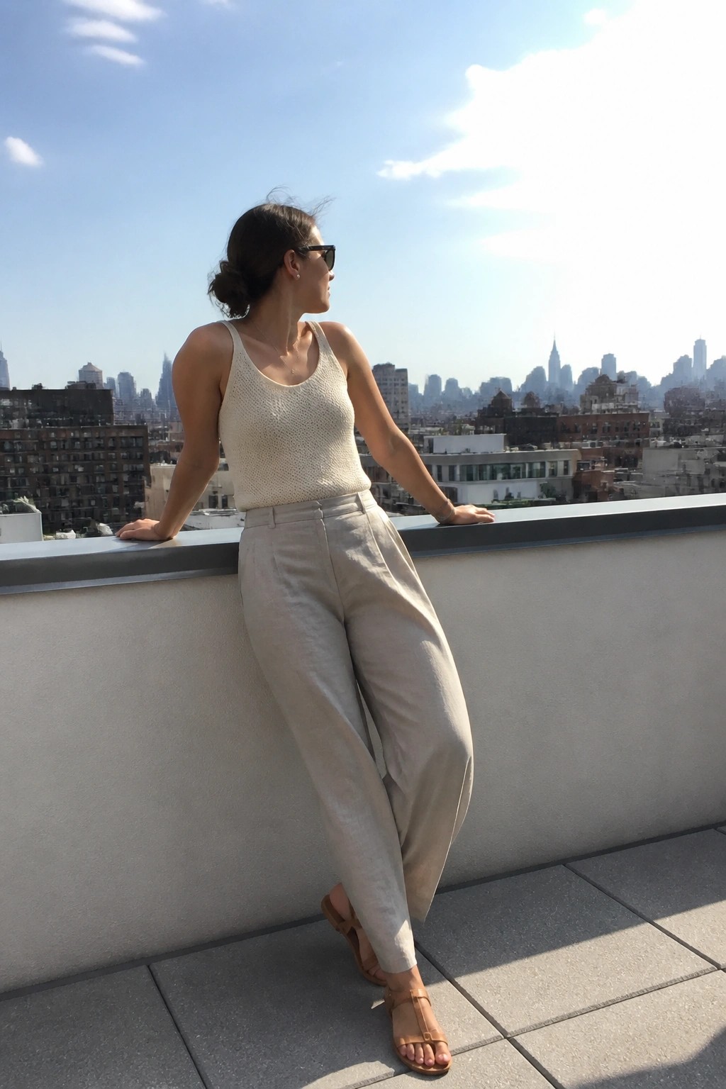 Woman in cream knit top and beige pants on rooftop overlooking city skyline