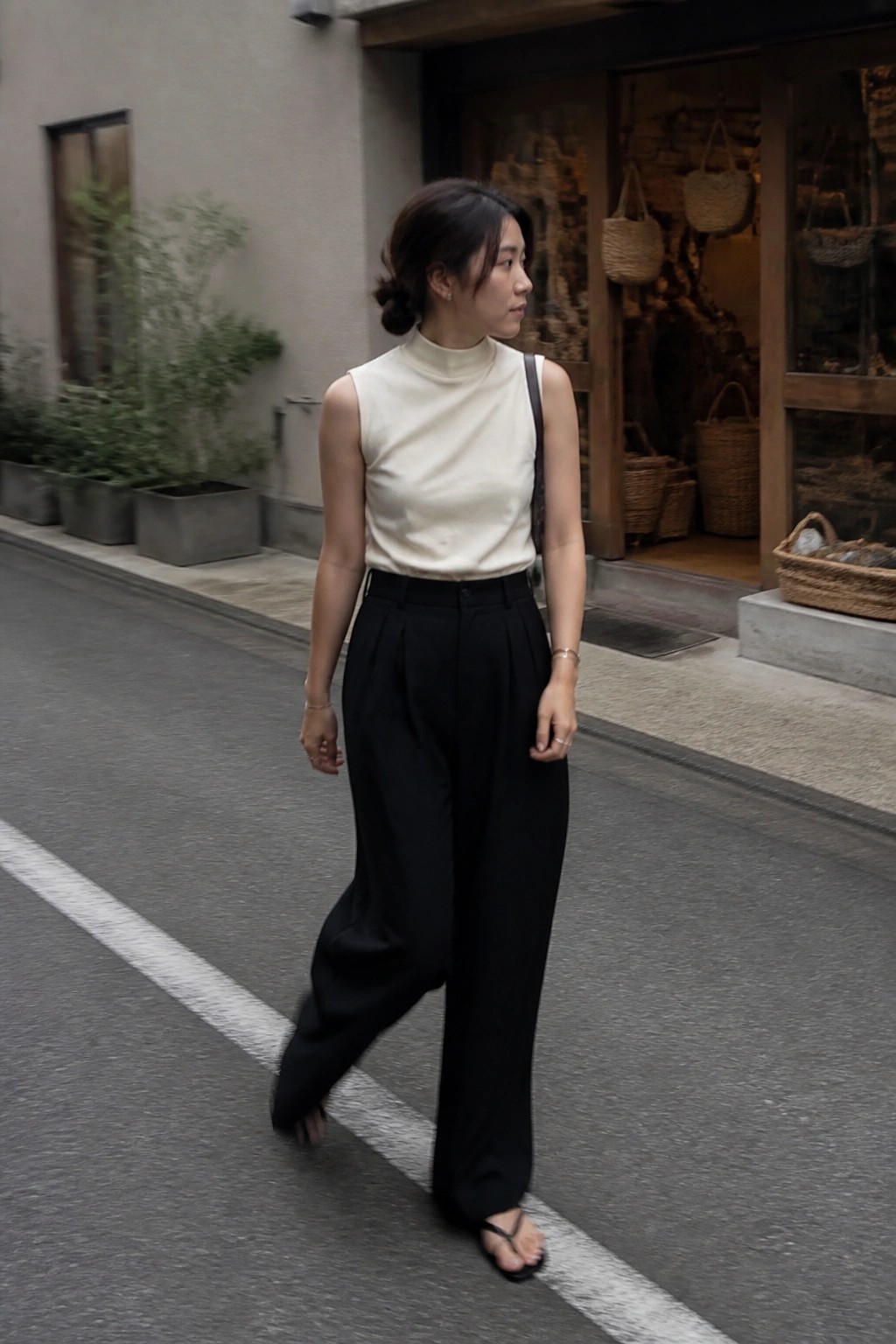 Woman in cream sleeveless turtleneck and black wide-leg pants walking on street