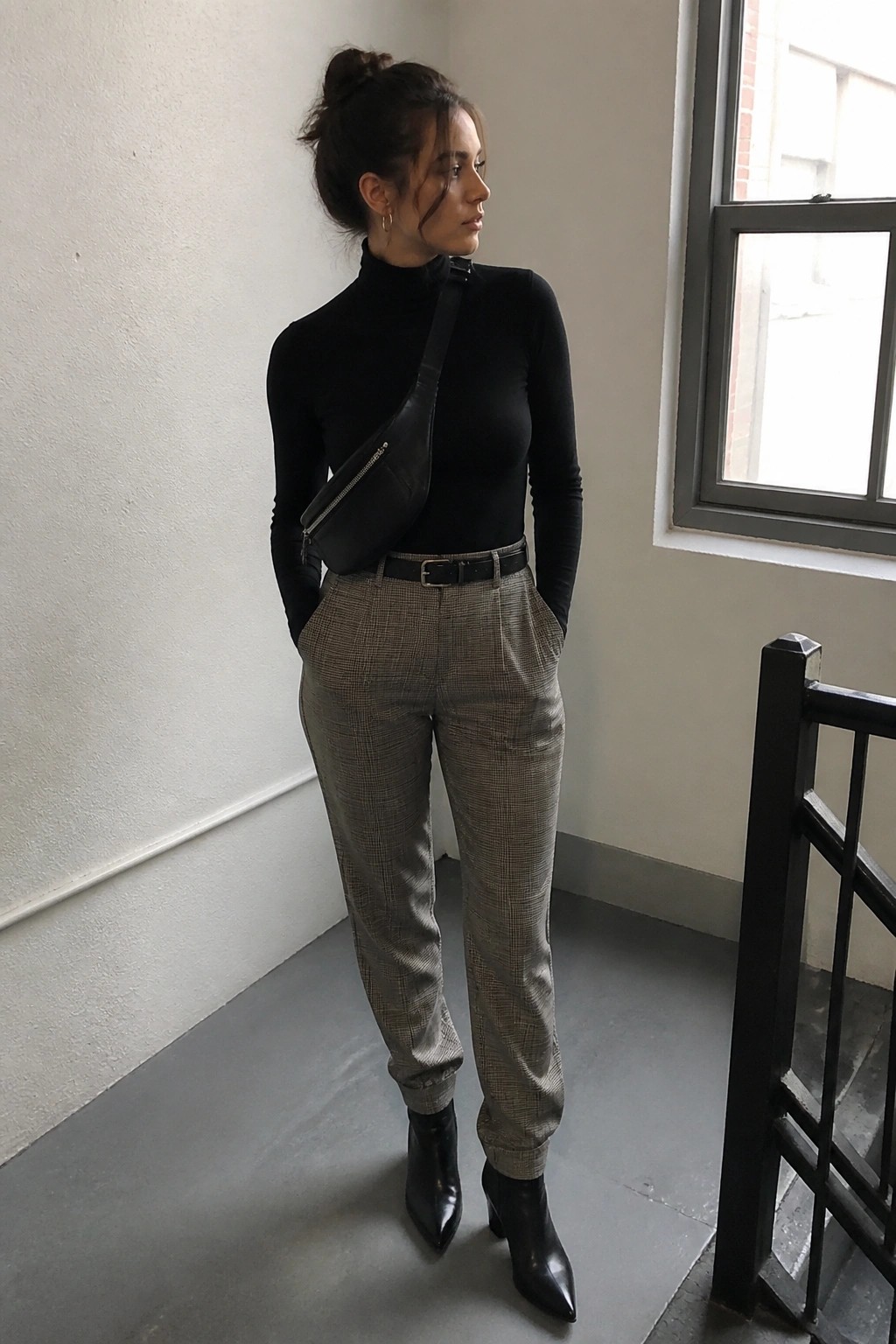 Woman in black turtleneck and plaid pants with crossbody bag indoors.