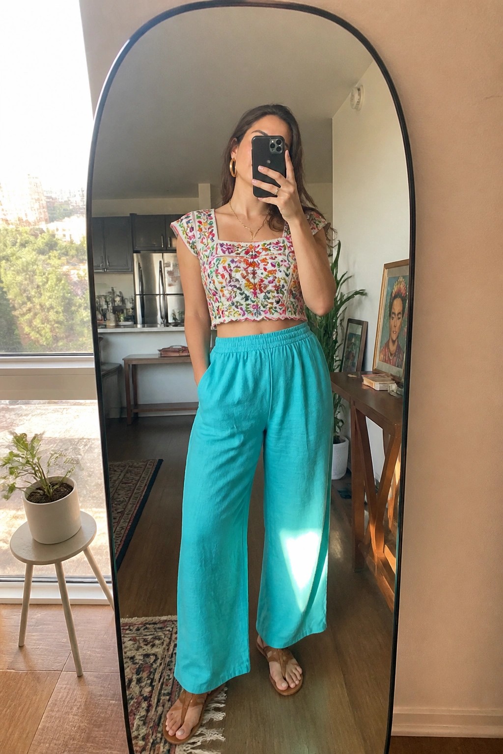 Woman in embroidered floral crop top and turquoise pants taking mirror selfie.