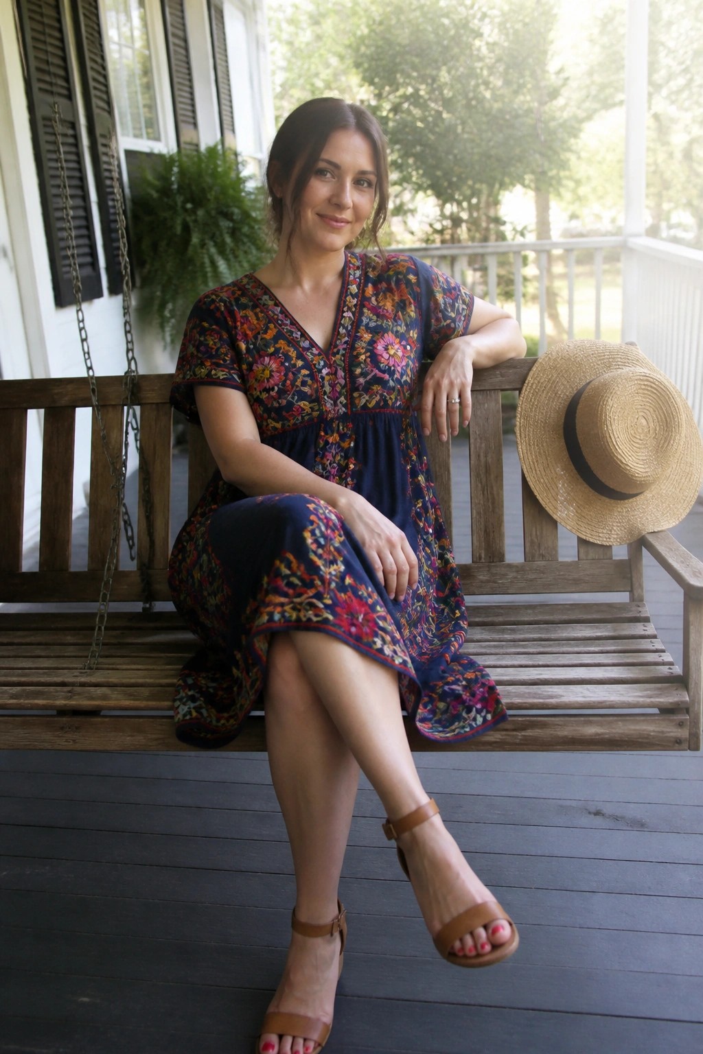 Woman in colorful embroidered dress on wooden porch swing beside straw hat