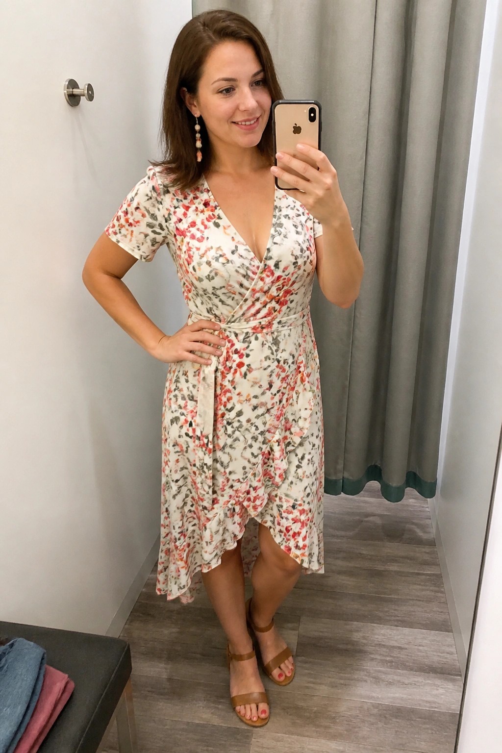 Woman in floral wrap dress taking mirror selfie in fitting room with sandals