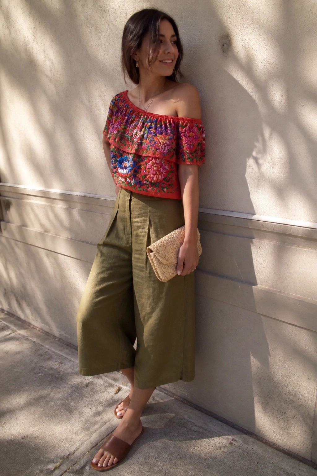 Woman in embroidered red off-shoulder top and olive culottes holding woven clutch