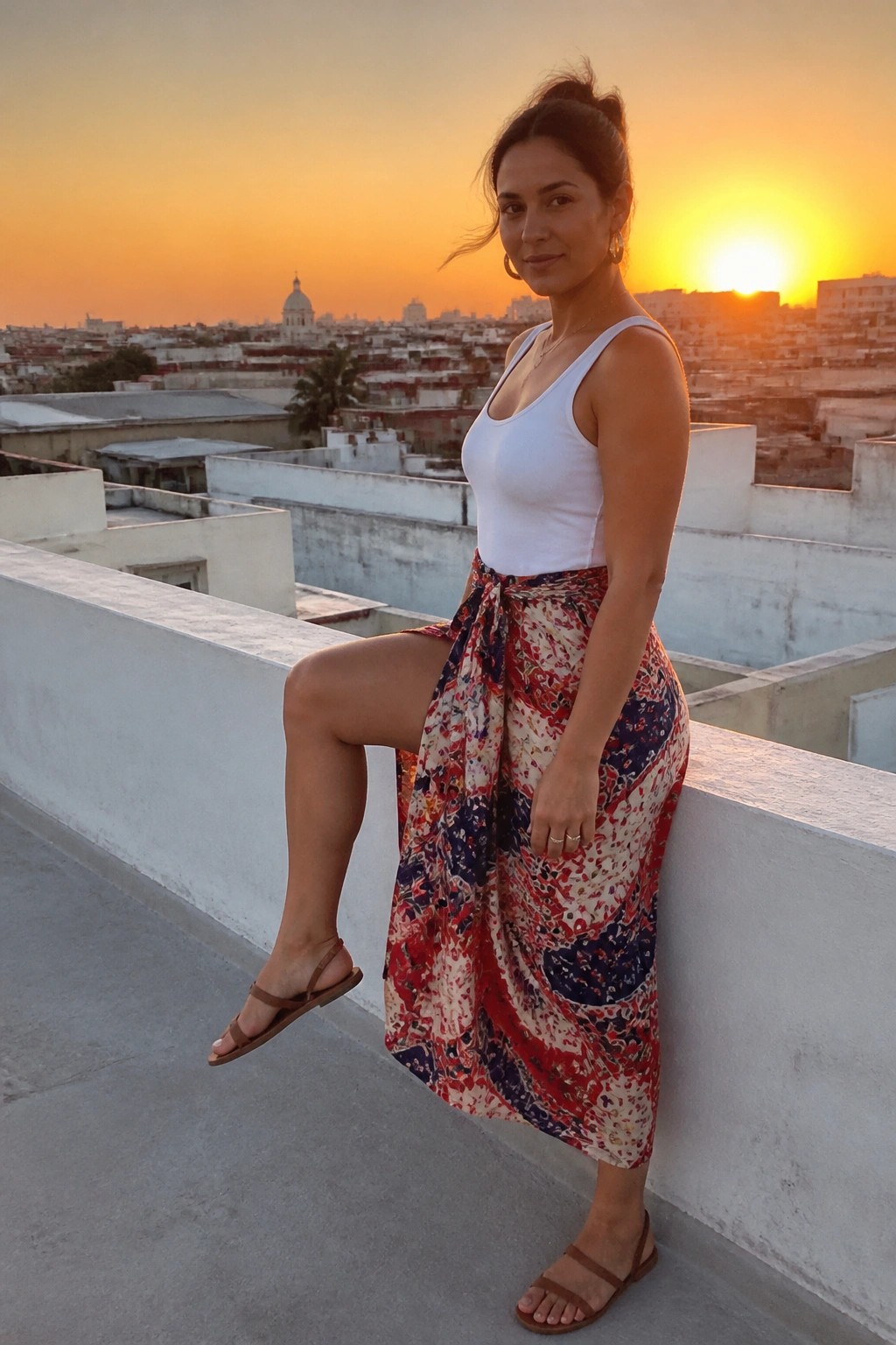 Woman in white top and floral skirt posing on rooftop at sunset