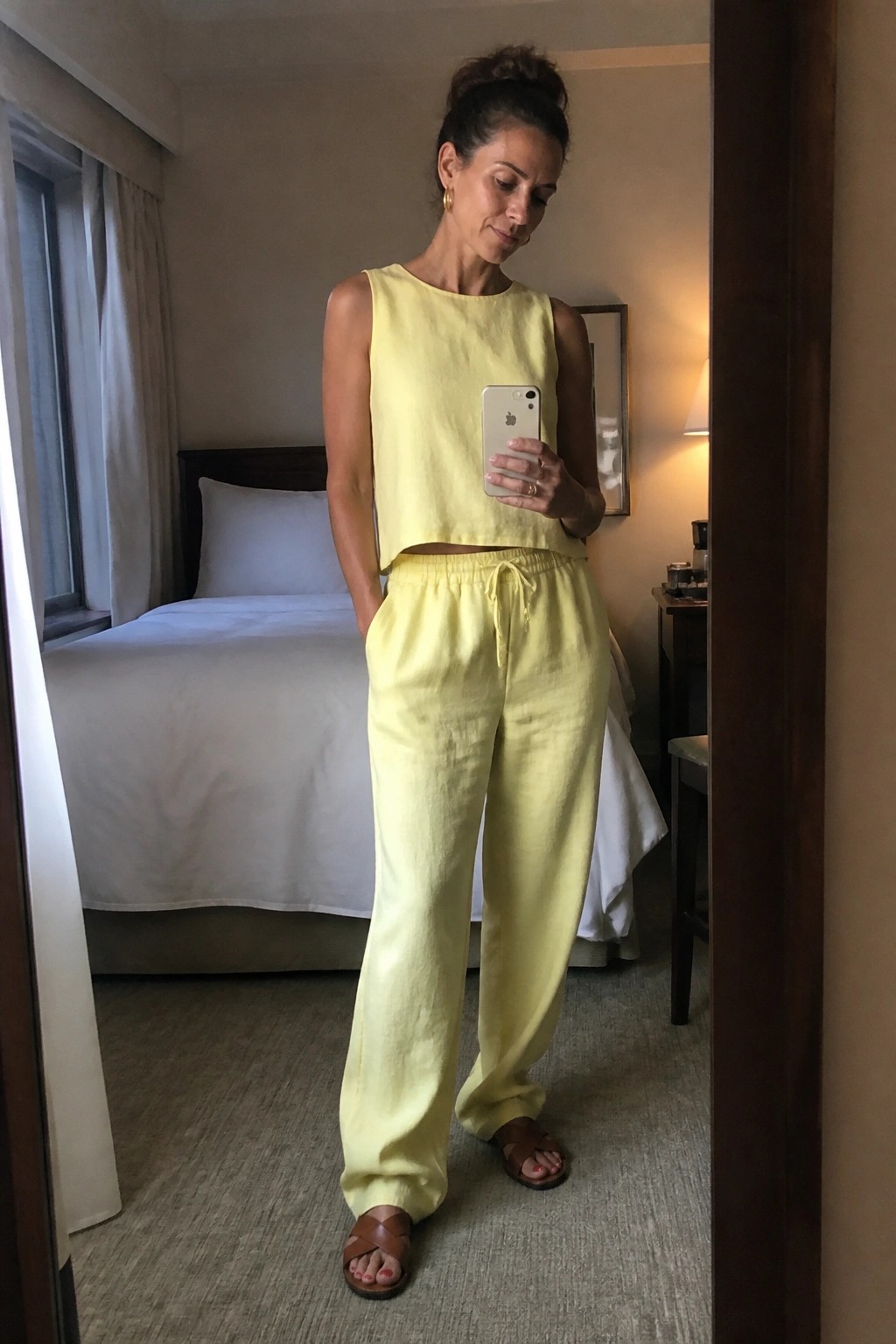 Woman in yellow linen crop top and pants taking mirror selfie in bedroom