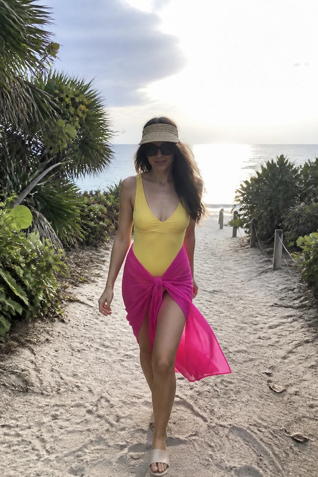 Woman in yellow swimsuit and pink sarong walking on sandy beach path