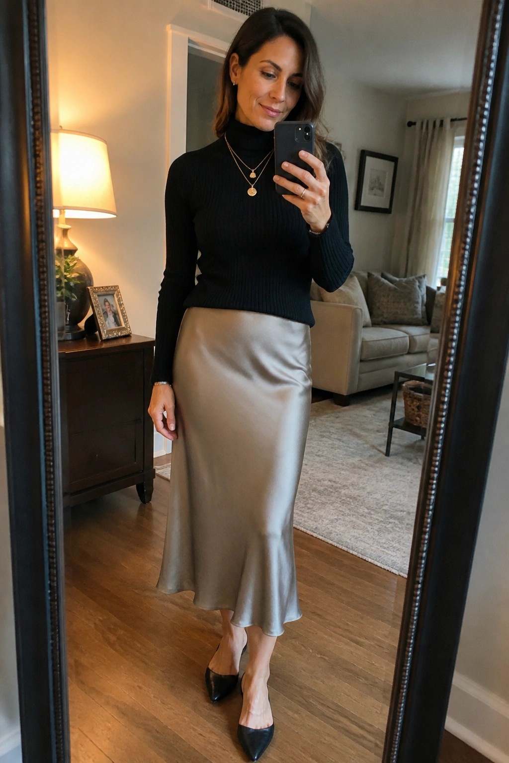 Woman in black turtleneck and beige satin skirt taking living room mirror selfie