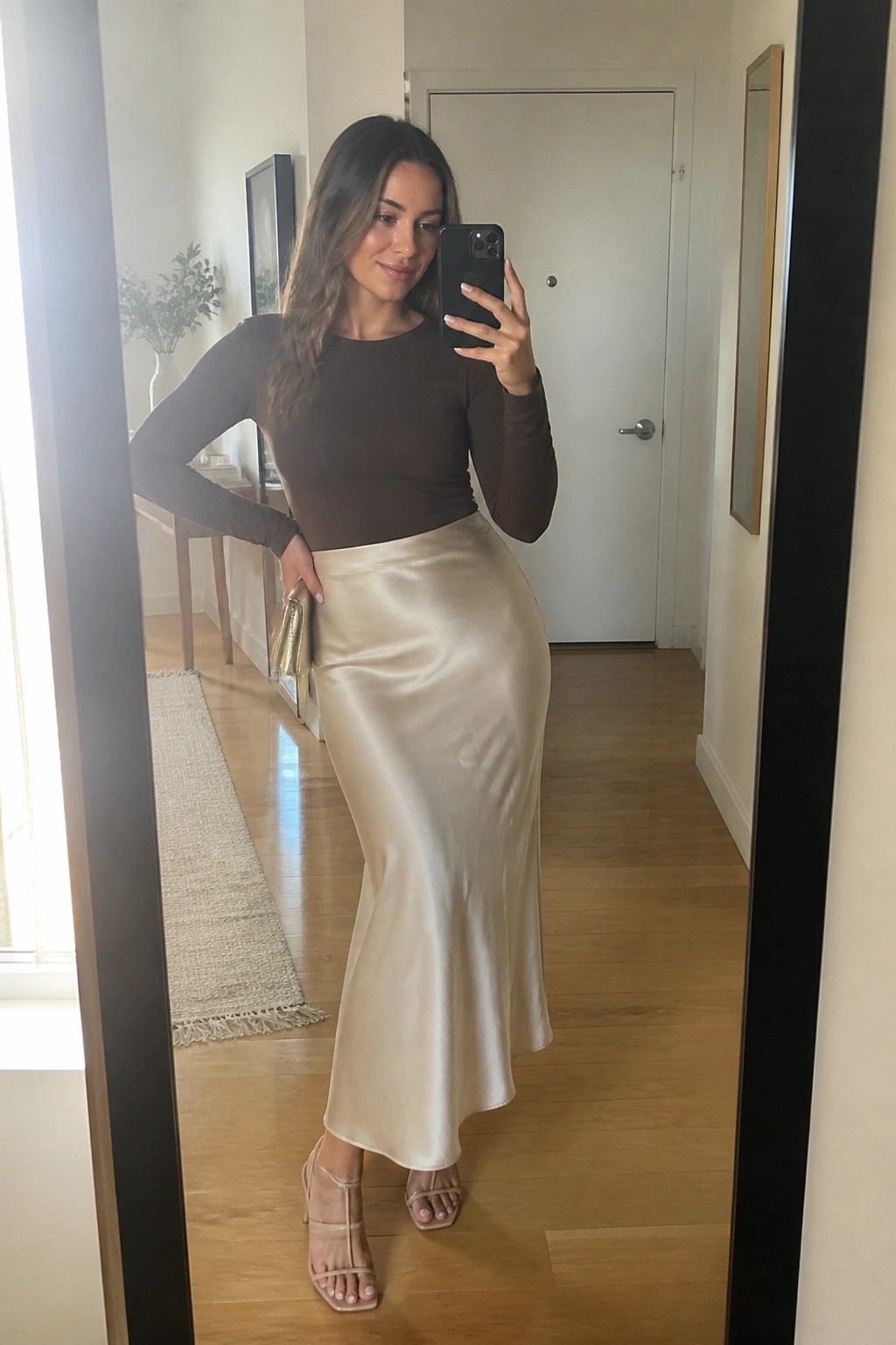 Woman in brown top and beige satin skirt taking mirror selfie with phone