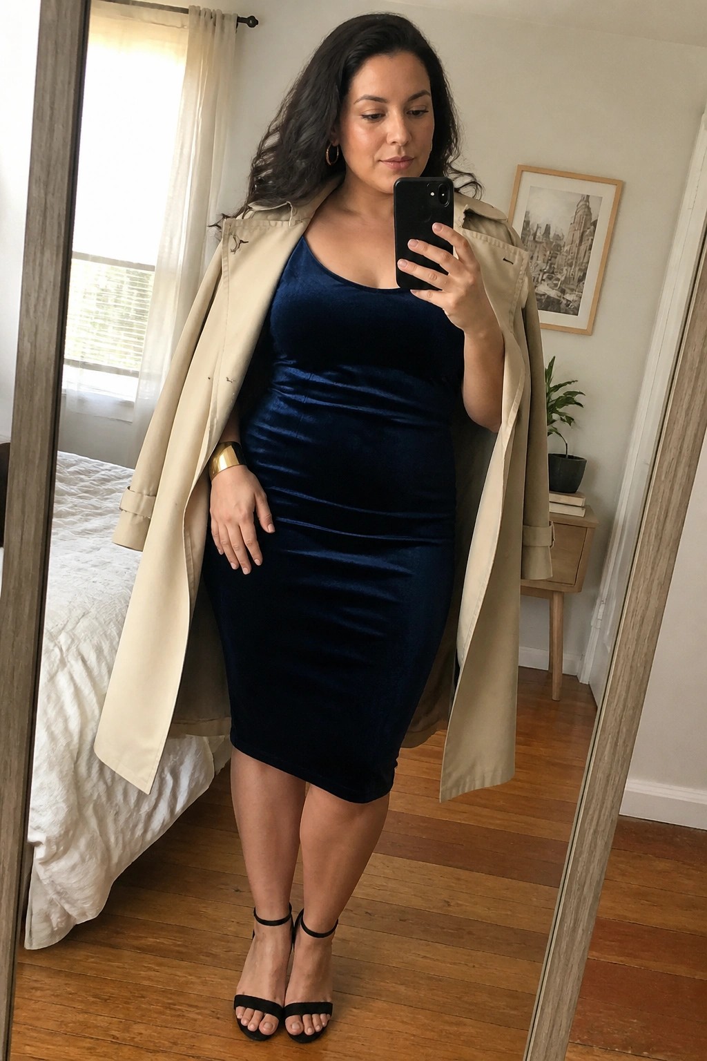 Woman in navy velvet dress and beige trench coat taking mirror selfie