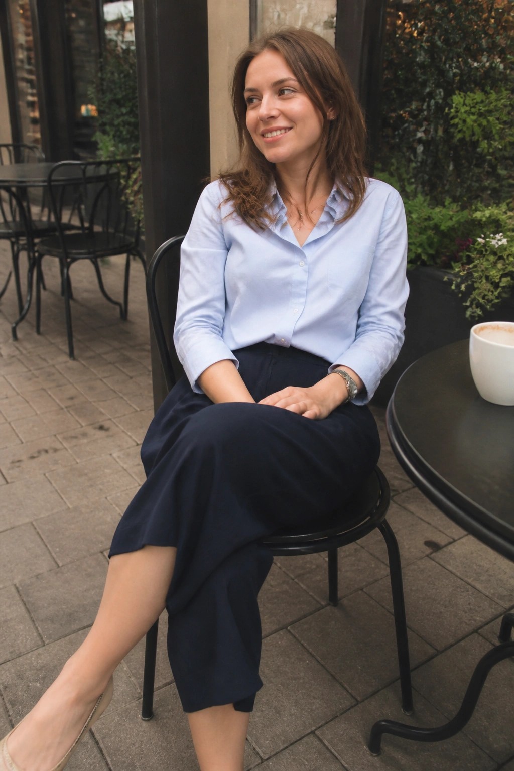 Woman in light blue shirt and navy skirt at outdoor cafe table with coffee