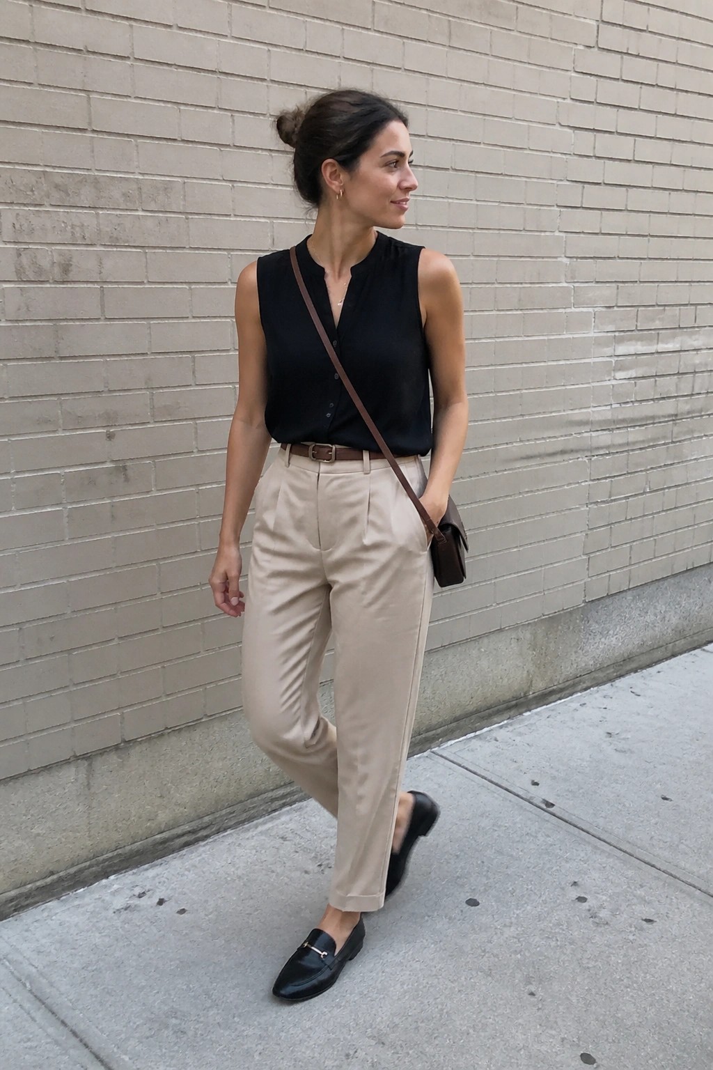 Woman in black sleeveless top and beige pants against brick wall