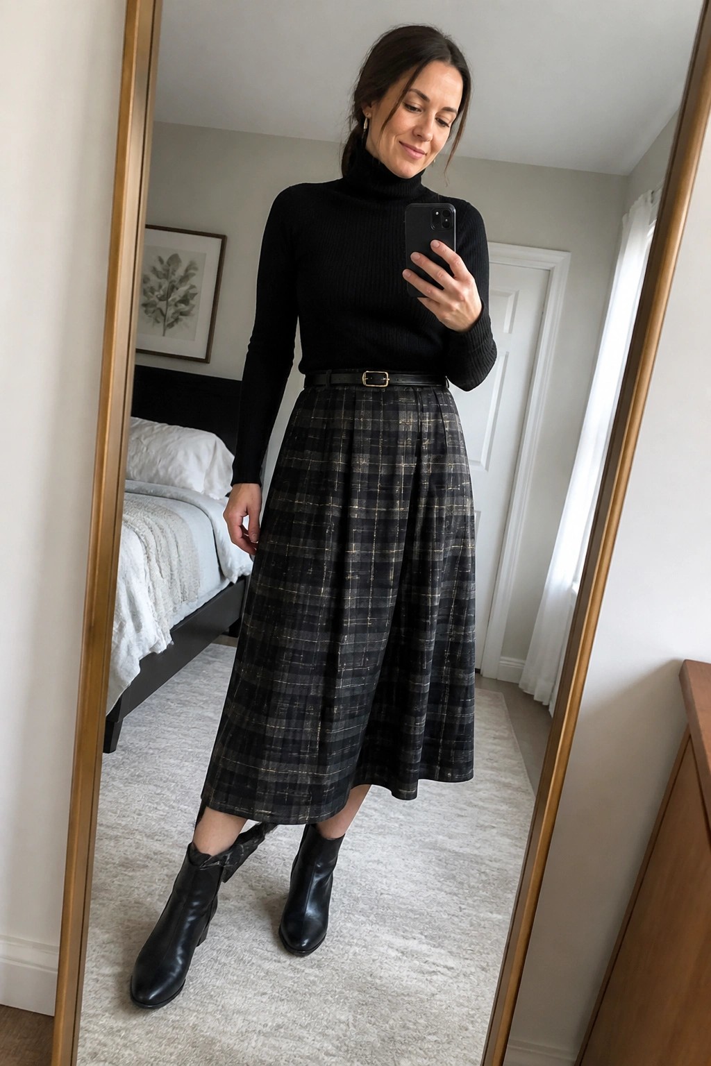 Woman in black turtleneck, plaid midi skirt, and ankle boots taking mirror selfie.