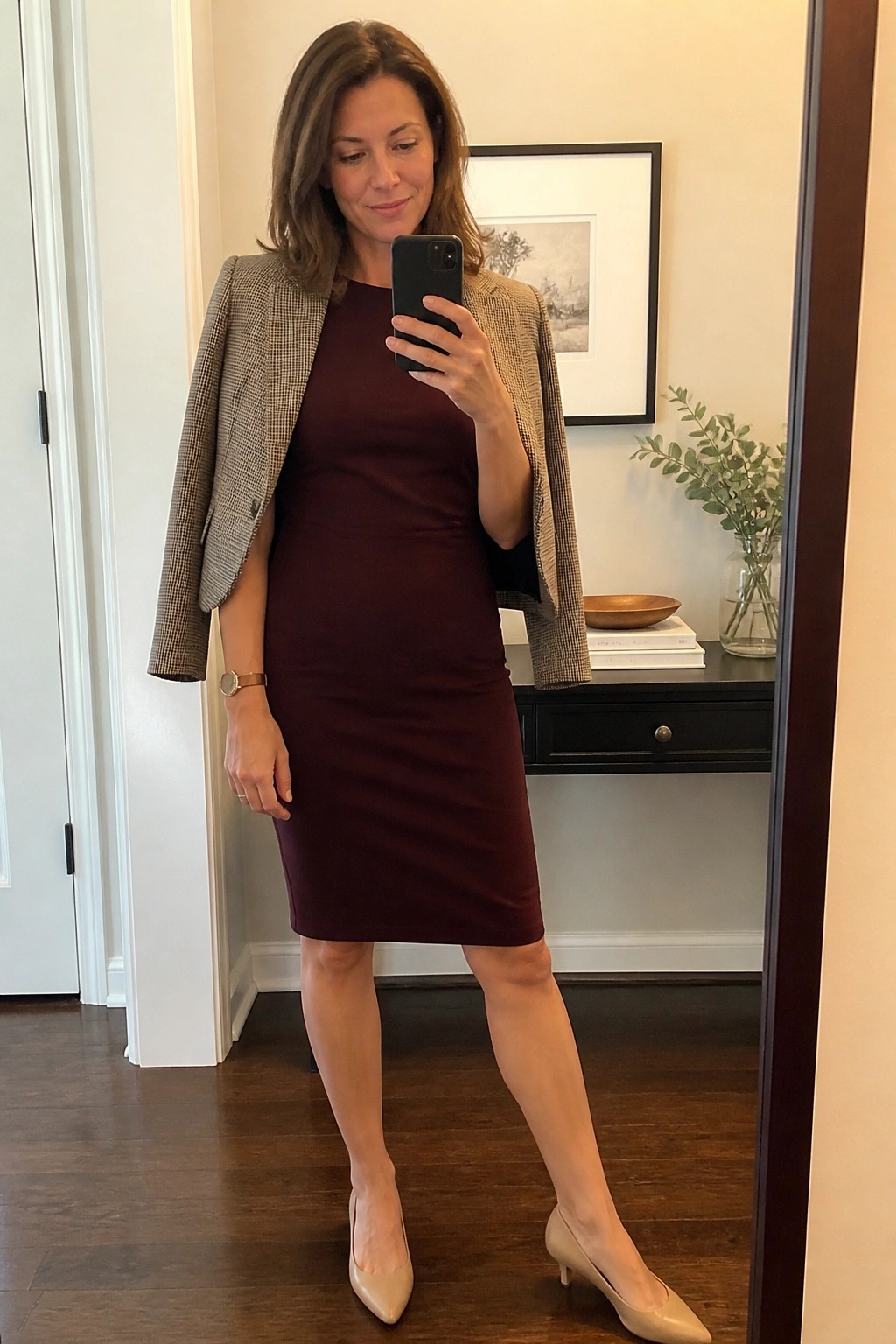 Woman in maroon dress and houndstooth blazer taking mirror selfie in beige heels