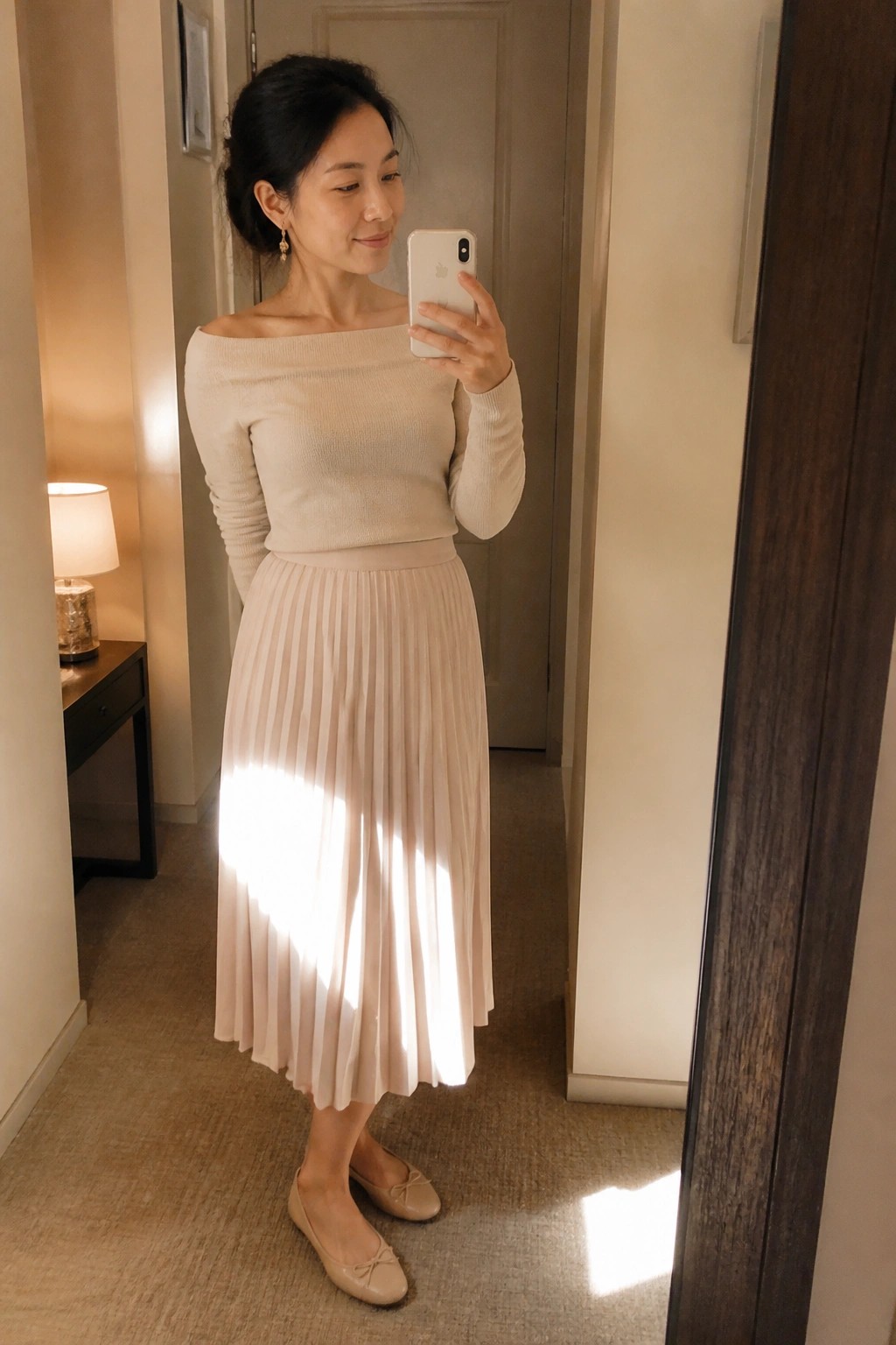 Woman in beige off-shoulder sweater and pleated skirt taking mirror selfie