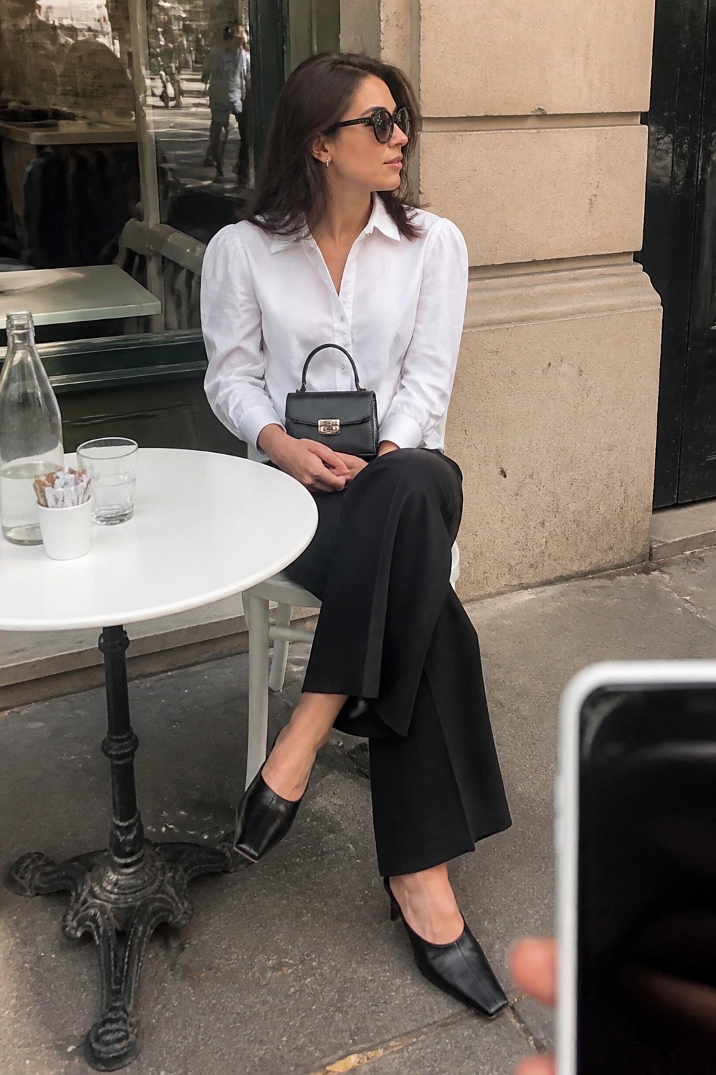Woman in white shirt and black pants at outdoor cafe holding black handbag
