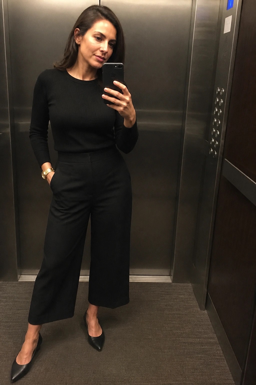 Woman in black outfit taking selfie inside elevator with smartphone