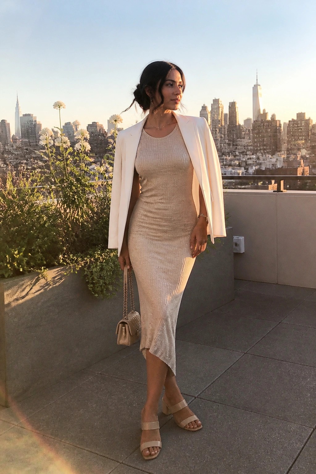 Woman in beige midi dress and white blazer on NYC rooftop at sunset