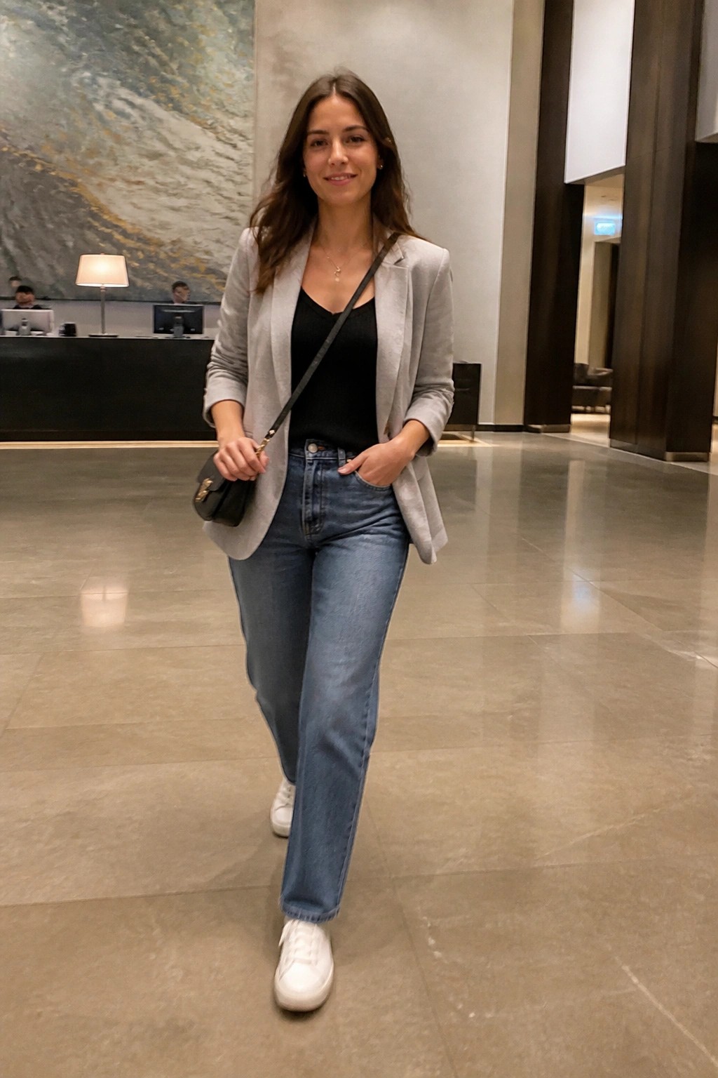 Woman in gray blazer and jeans smiling in modern hotel lobby