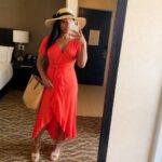 Woman in red wrap dress, straw hat, holding phone and woven bag in mirror