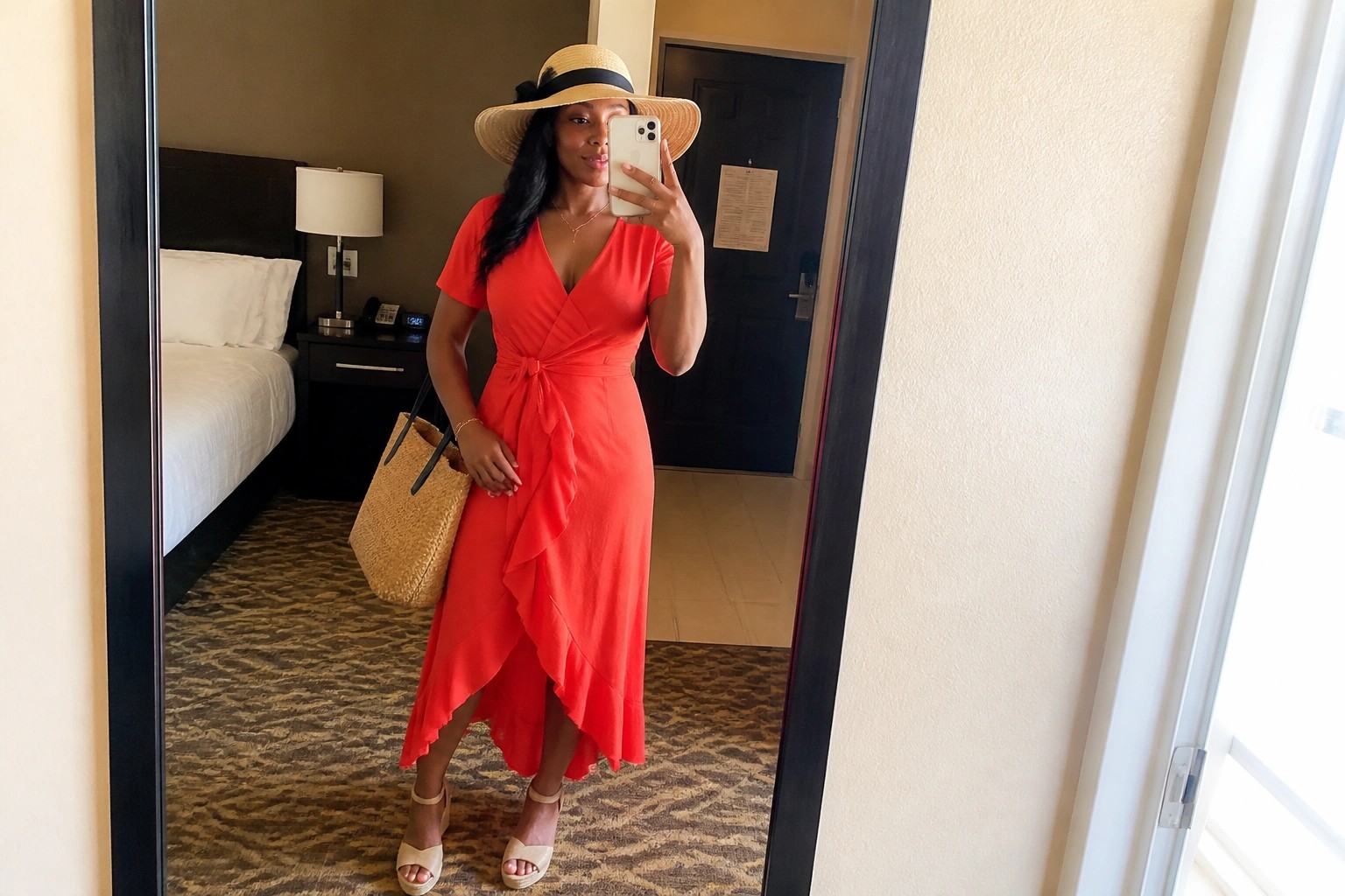 Woman in red wrap dress, straw hat, holding phone and woven bag in mirror