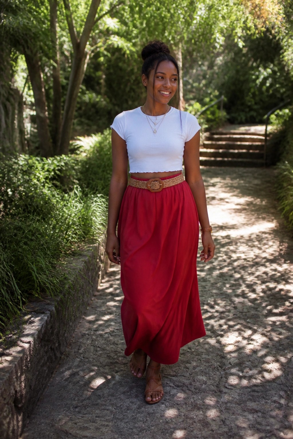 Woman in white crop top and flowing red skirt on sunny forest path