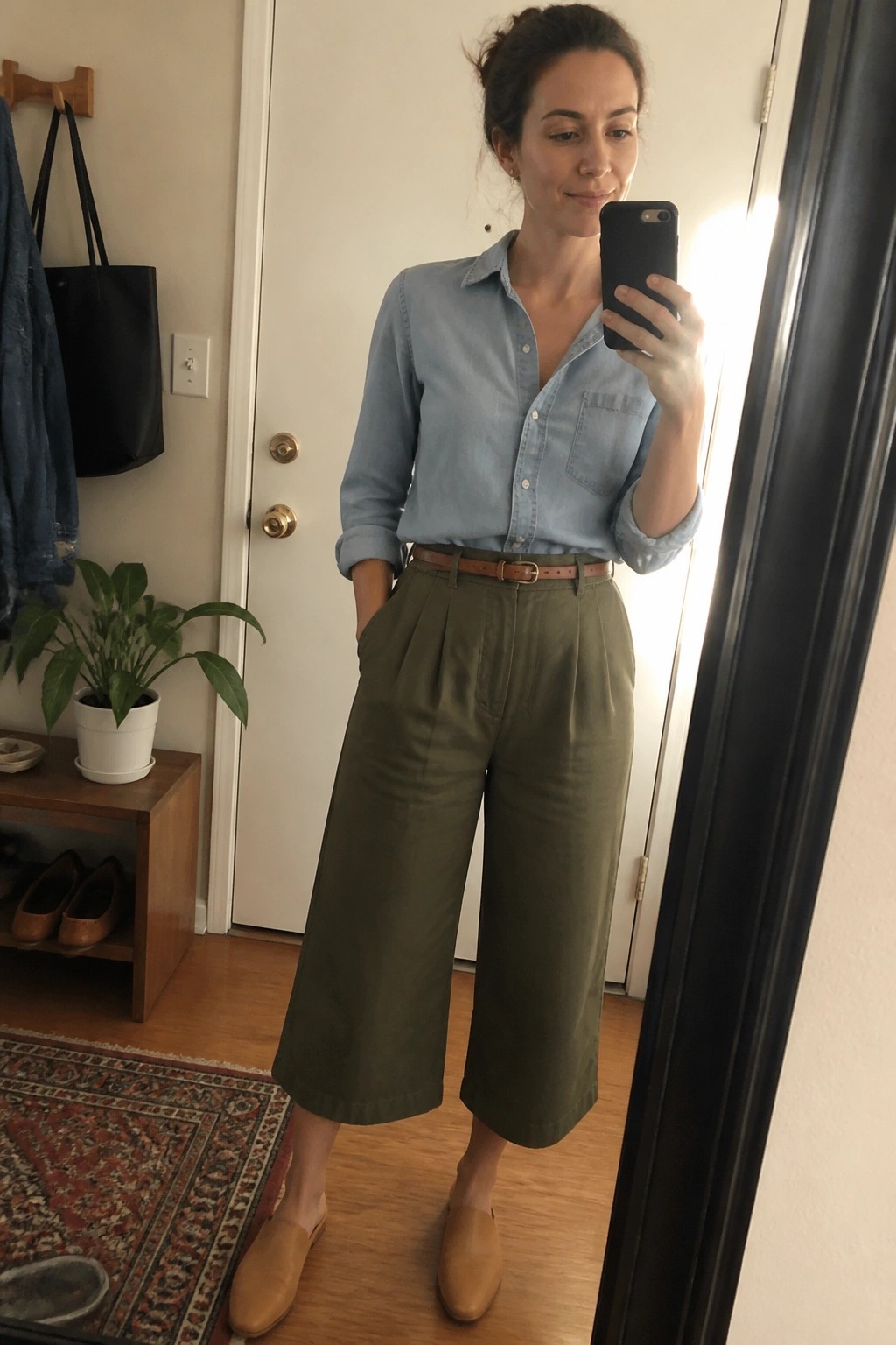 Woman in blue shirt and olive culottes taking mirror selfie indoors