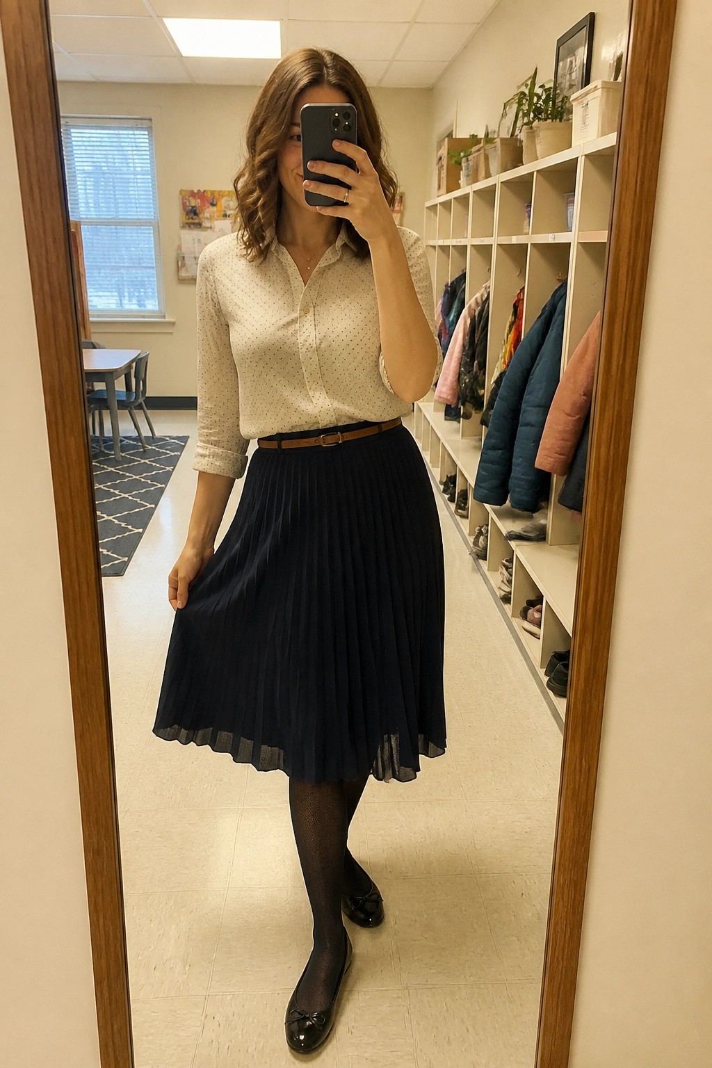 Woman wearing a cream polka dot button-up shirt tucked into a navy pleated midi skirt with brown belt, black tights, and black bow flats.