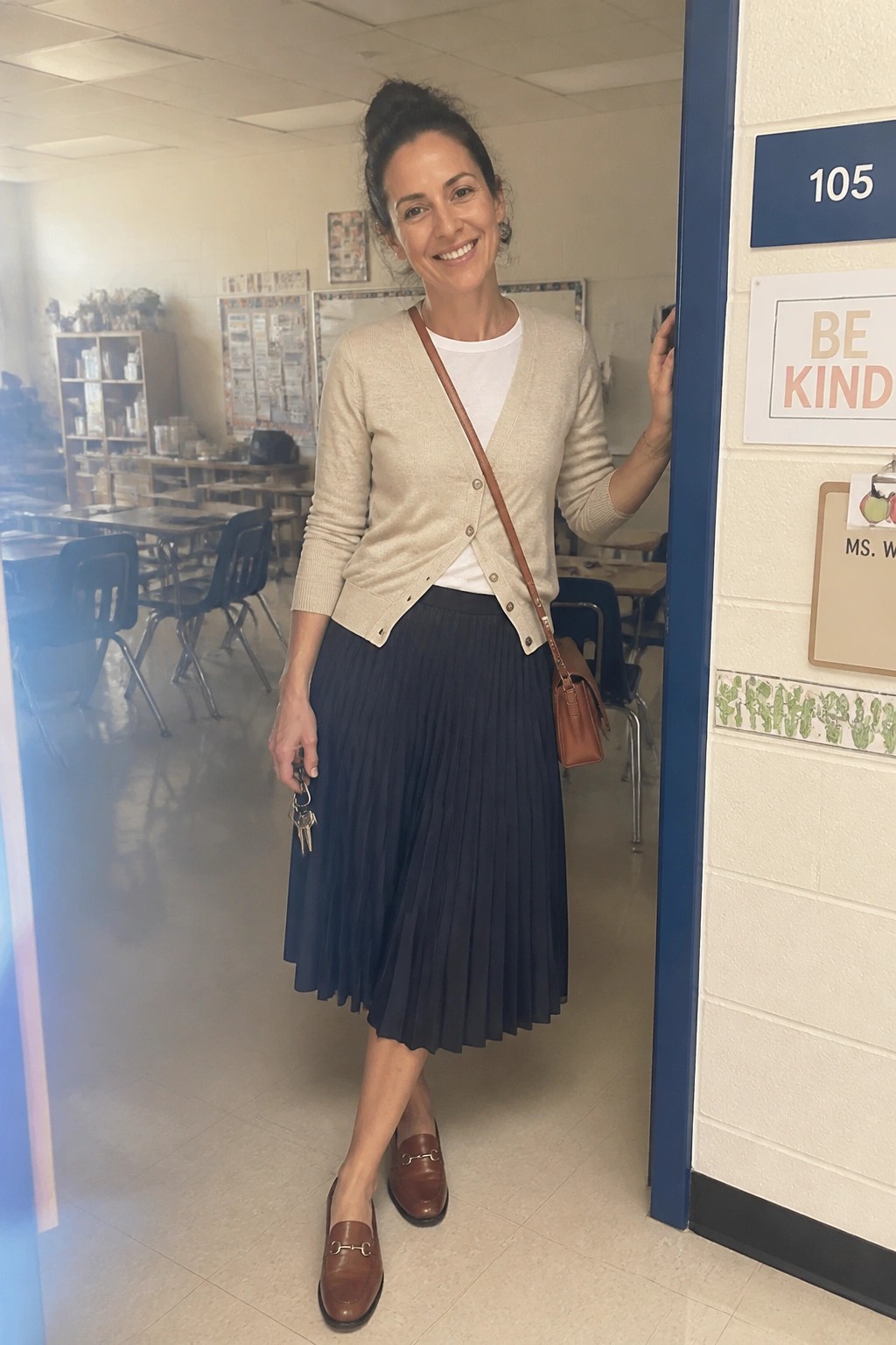 Smiling woman in beige cardigan and navy pleated skirt at classroom doorway