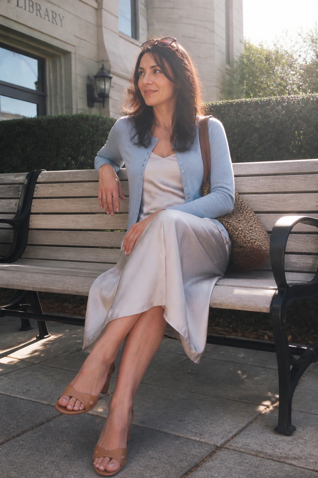 Woman in light blue cardigan and satin dress on library bench with leopard bag
